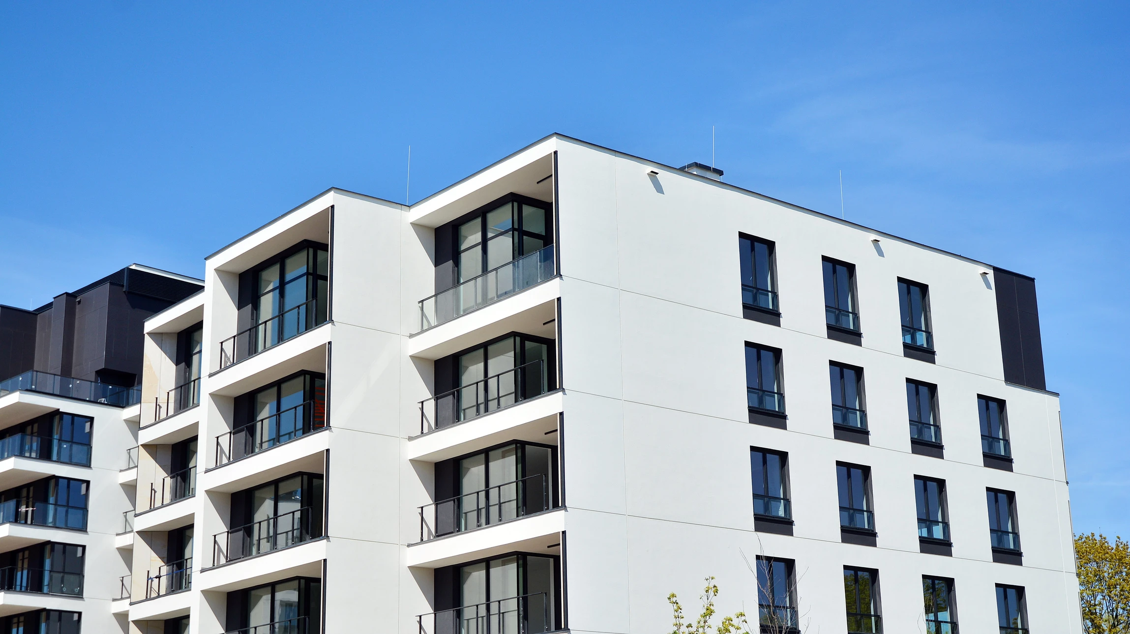 Façade d'immeuble résidentiel moderne avec balcons et grandes baies vitrées sous ciel bleu dégagé