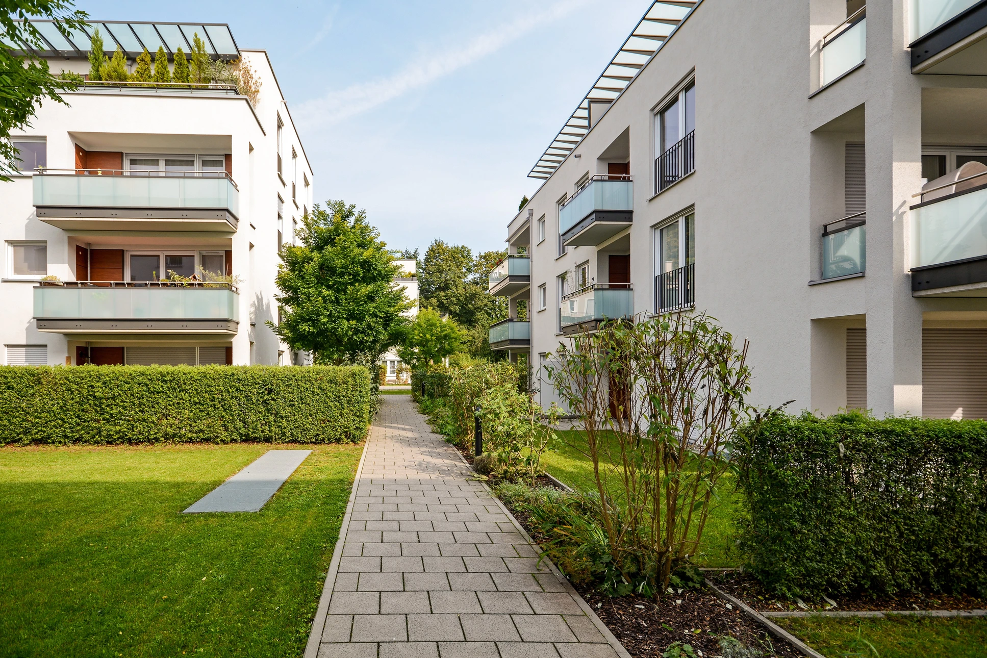 Ensemble résidentiel moderne avec immeubles d'appartements blancs à balcons vitrés, espaces verts paysagers et allée pavée centrale