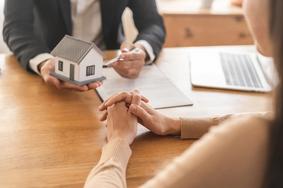 Un agent immobilier professionnel, debout dans le salon vide d'un nouvel appartement, donne les clés de maison à un couple marié heureux
